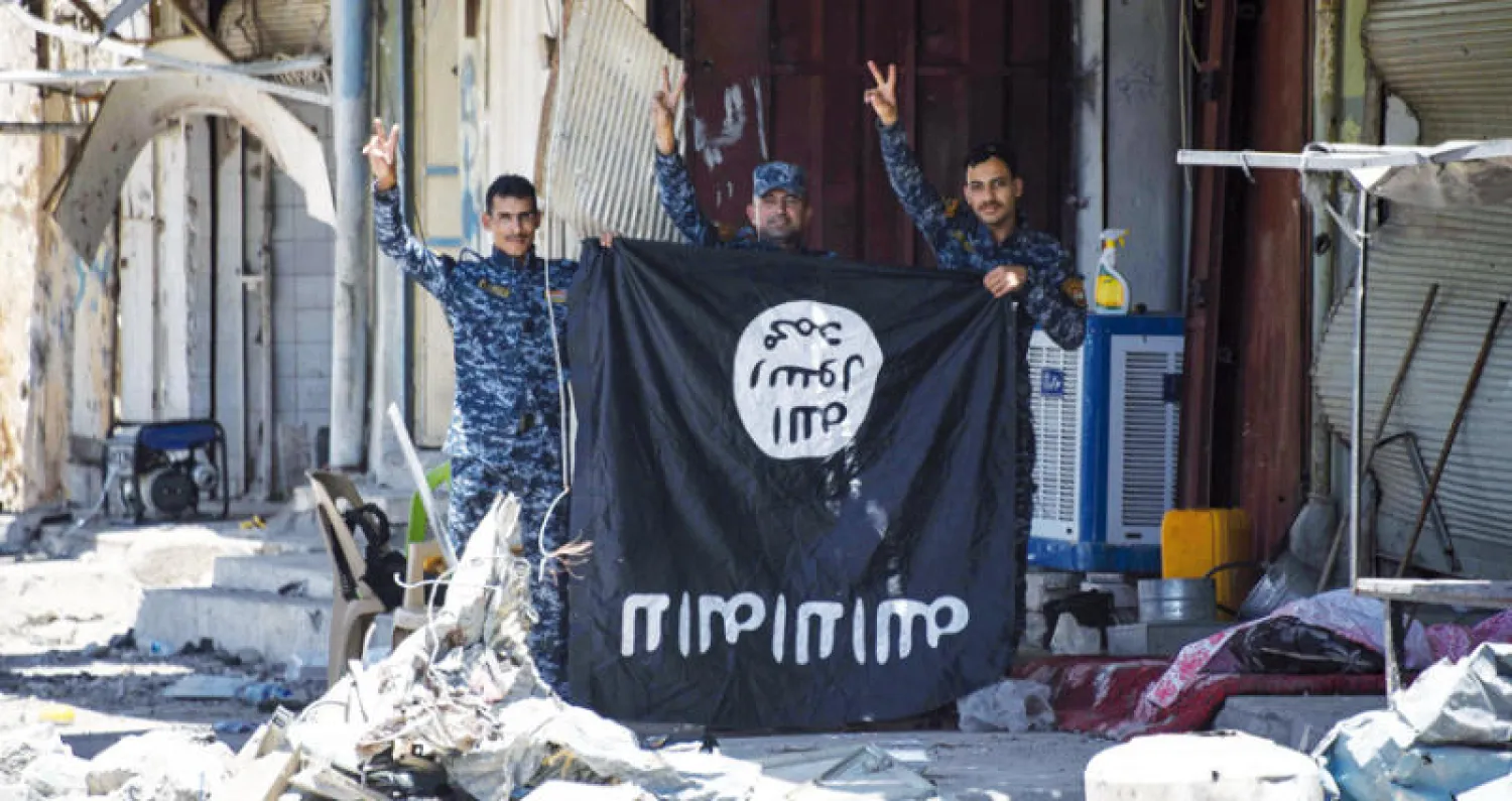 جنود من القوات العراقية يرفعون علما كان يستخدمه «الدواعش} عقب طردهم من الموصل (ا ف ب)