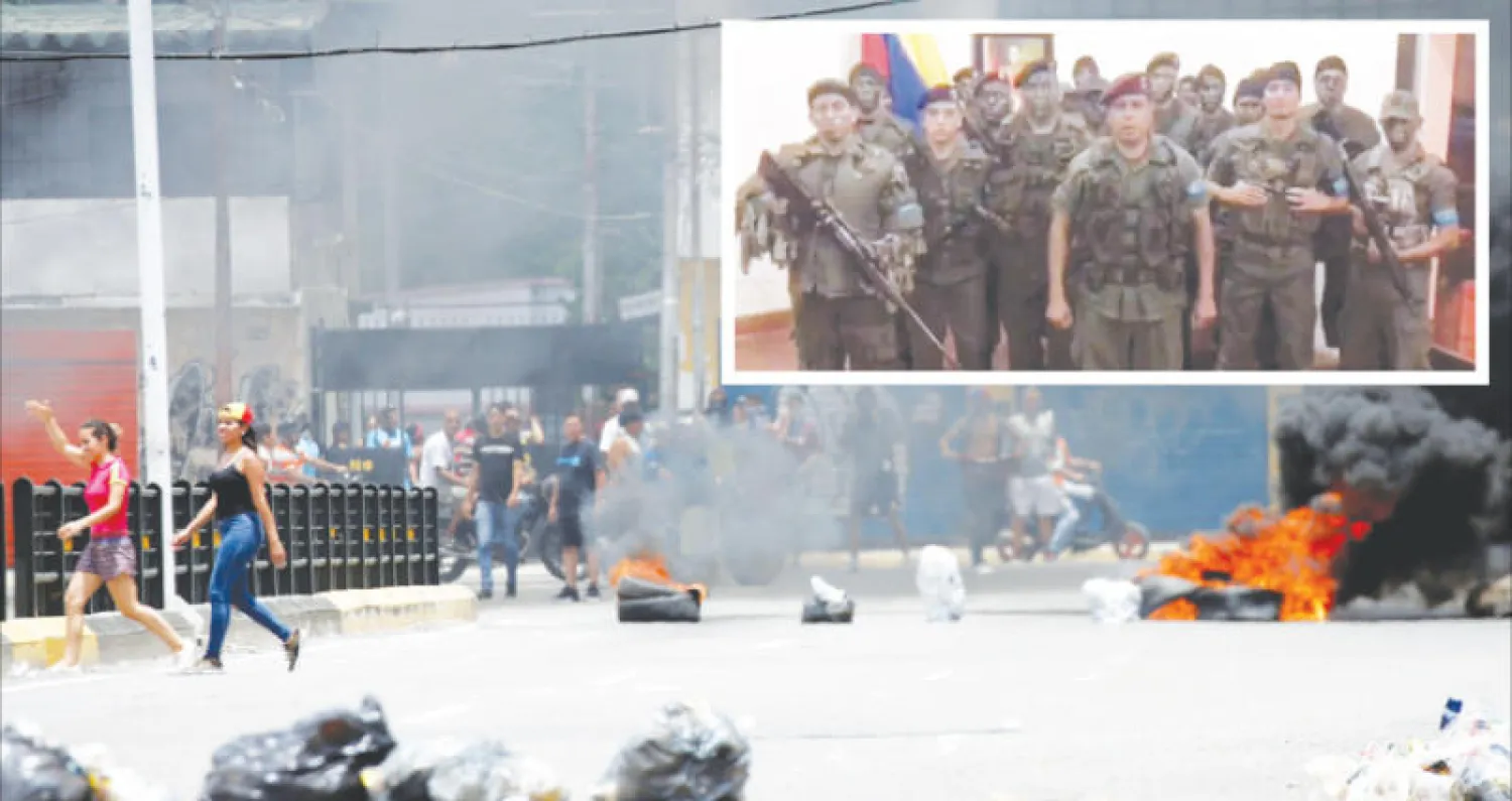 سكان يمرون أمام حواجز أقامها محتجون في فالنسيا أمس (رويترز) وفي الإطار لقطة من فيديو بث لرجل يعلن عن «تمرد عسكري» في المدينة (أ.ف.ب)