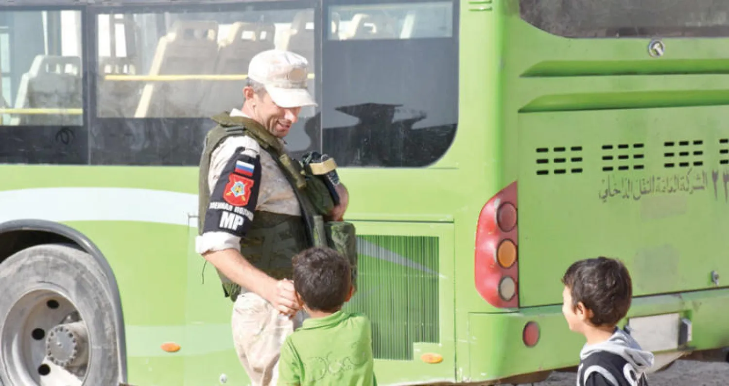 طفلان يتحدثات لعنصر من الشرطة الروسية في مركز للنازحين بجبرين قرب حلب (إ ف ب)