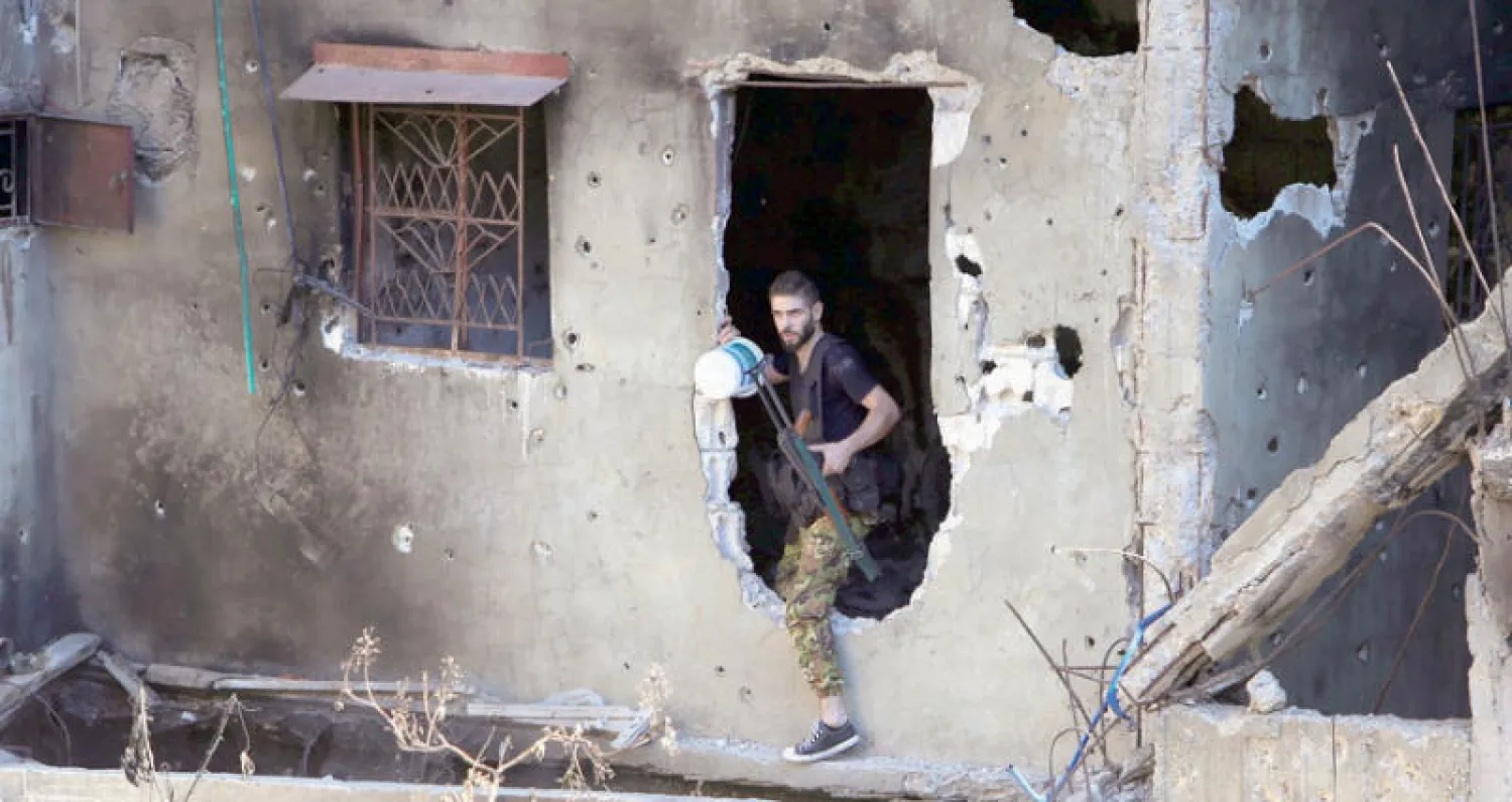 مقاتل من حركة فتح يجتاز فتحة تسببت فيها نيران المعارك بمخيم عين الحلوة الفلسطيني (رويترز)