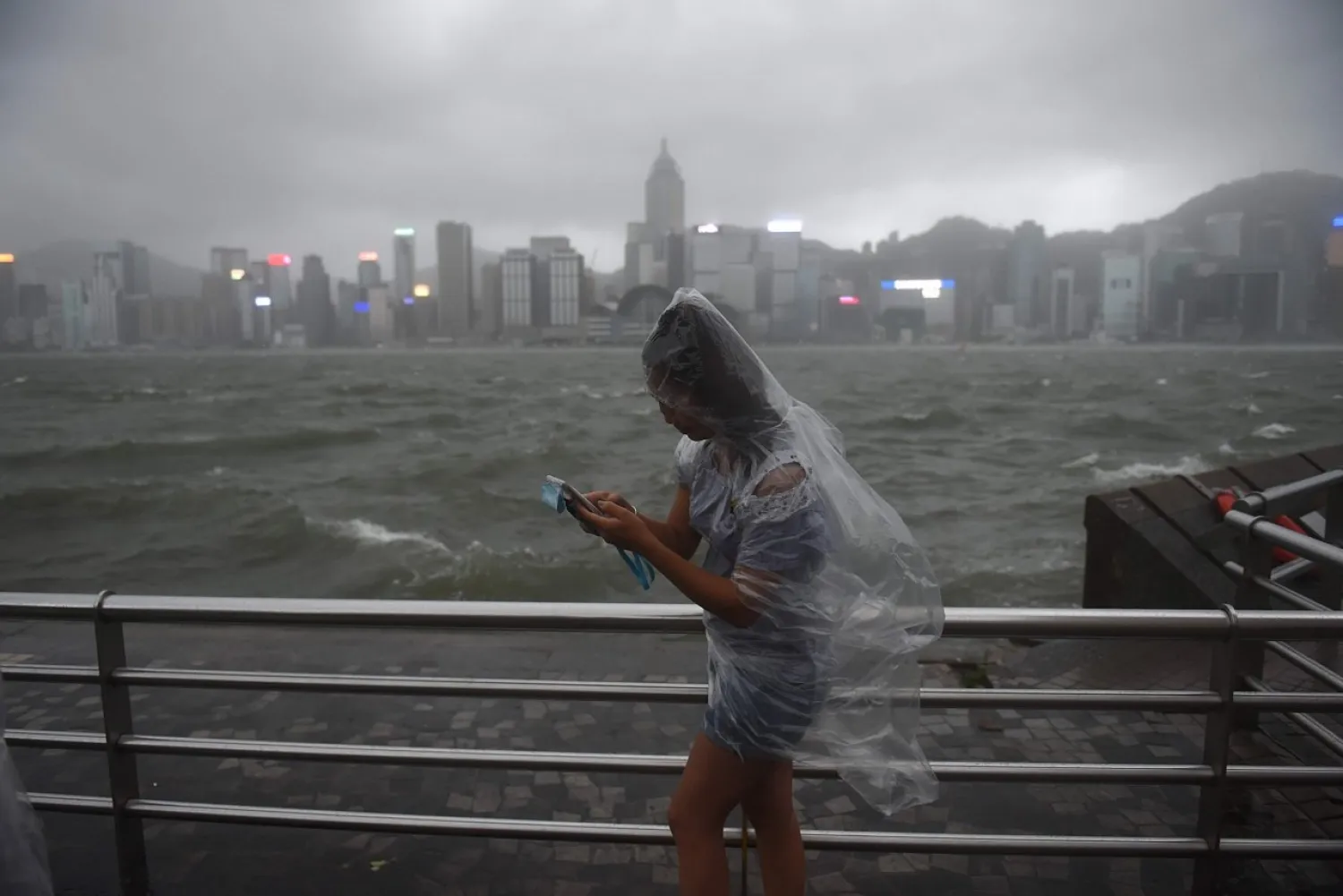 A woman uses her phone while wearing a plastic poncho along Victoria Harbour during heavy winds and rain brought on by Typhoon Hato in Hong Kong on August 23, 2017. AFP PHOTO 