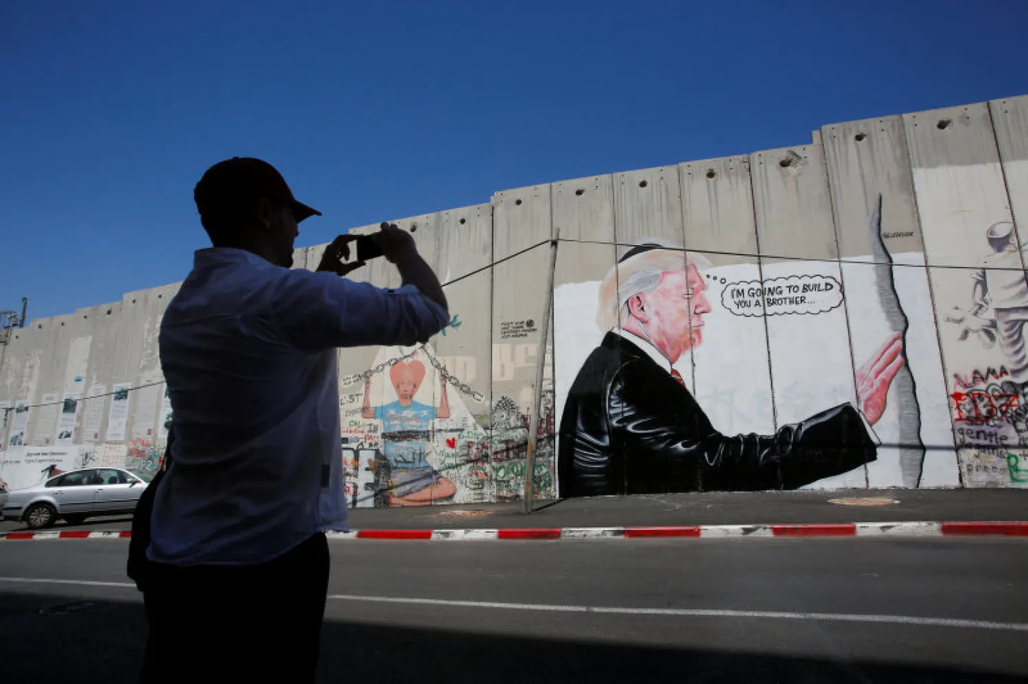 A man takes a photo of a graffiti depicting US President Donald Trump on the controversial Israeli barrier in the West Bank town of Bethlehem August 4, 2017. Reuters 