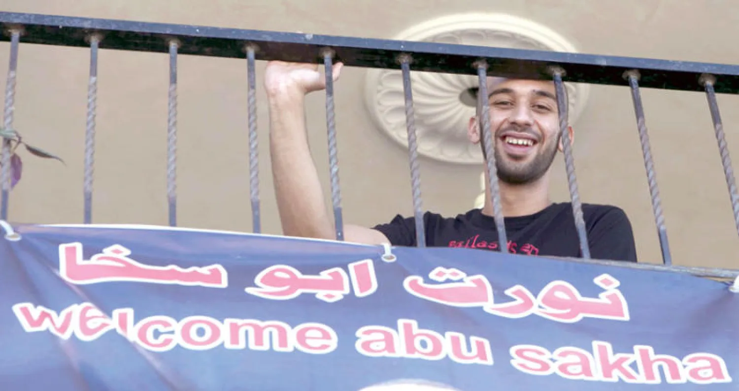 مهرج فلسطيني يقف بجانب ملصق يحمل صورته بمدينة جنين بالضفة بعد الإفراج الإداري عنه أمس (أ.ف.ب)