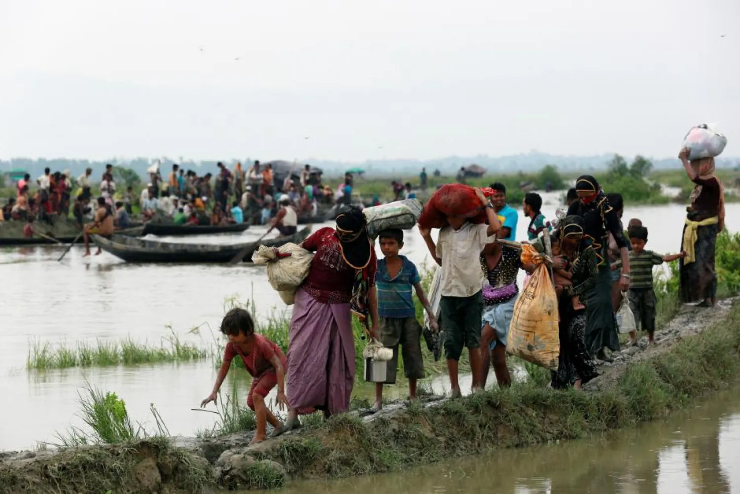 Rohingya refugees walk on a muddy path as others travel on a boat after crossing the Bangladesh-Myanmar border, in Teknaf, Bangladesh, September 6, 2017. REUTERS/Danish Siddiqui