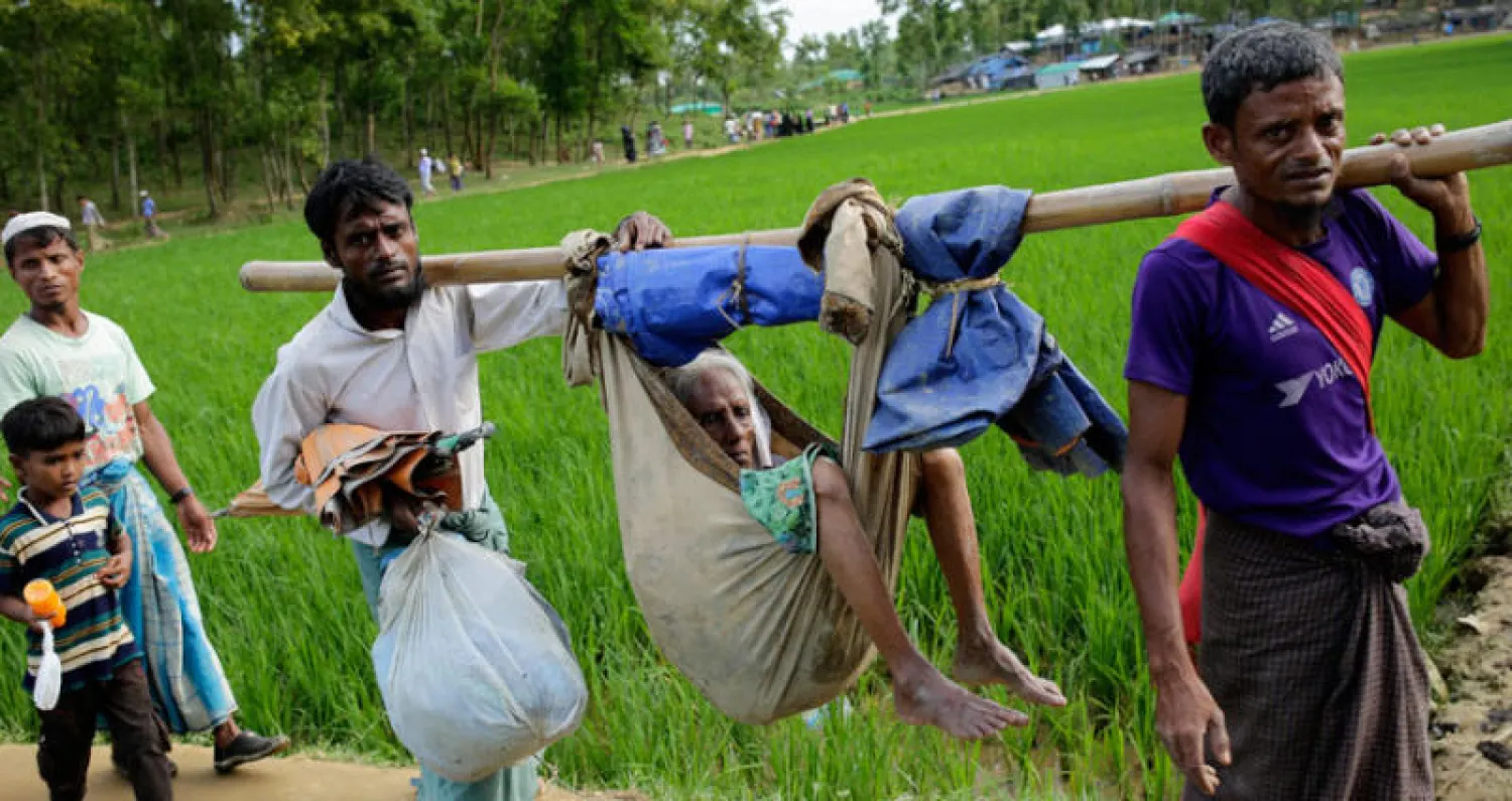 لاجئان من أقلية الروهينغا يحملان أمهما في الطريق إلى مخيم مؤقت بمنطقة كوكس بازار في بنغلاديش أمس (إ.ب.أ)