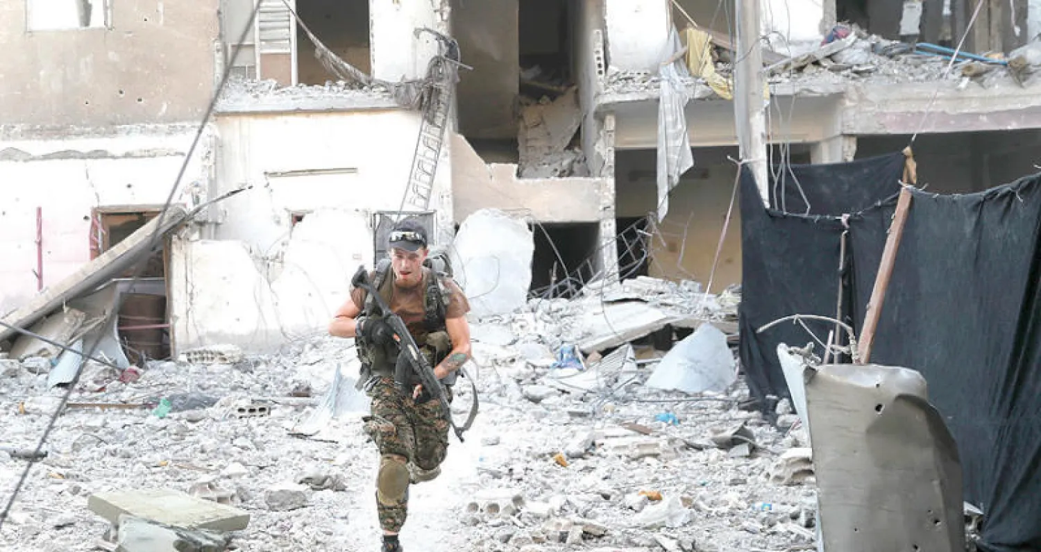 مقاتل من قوات سوريا الديمقراطية أمام مبنى مهدم في الرقة (أ.ب)