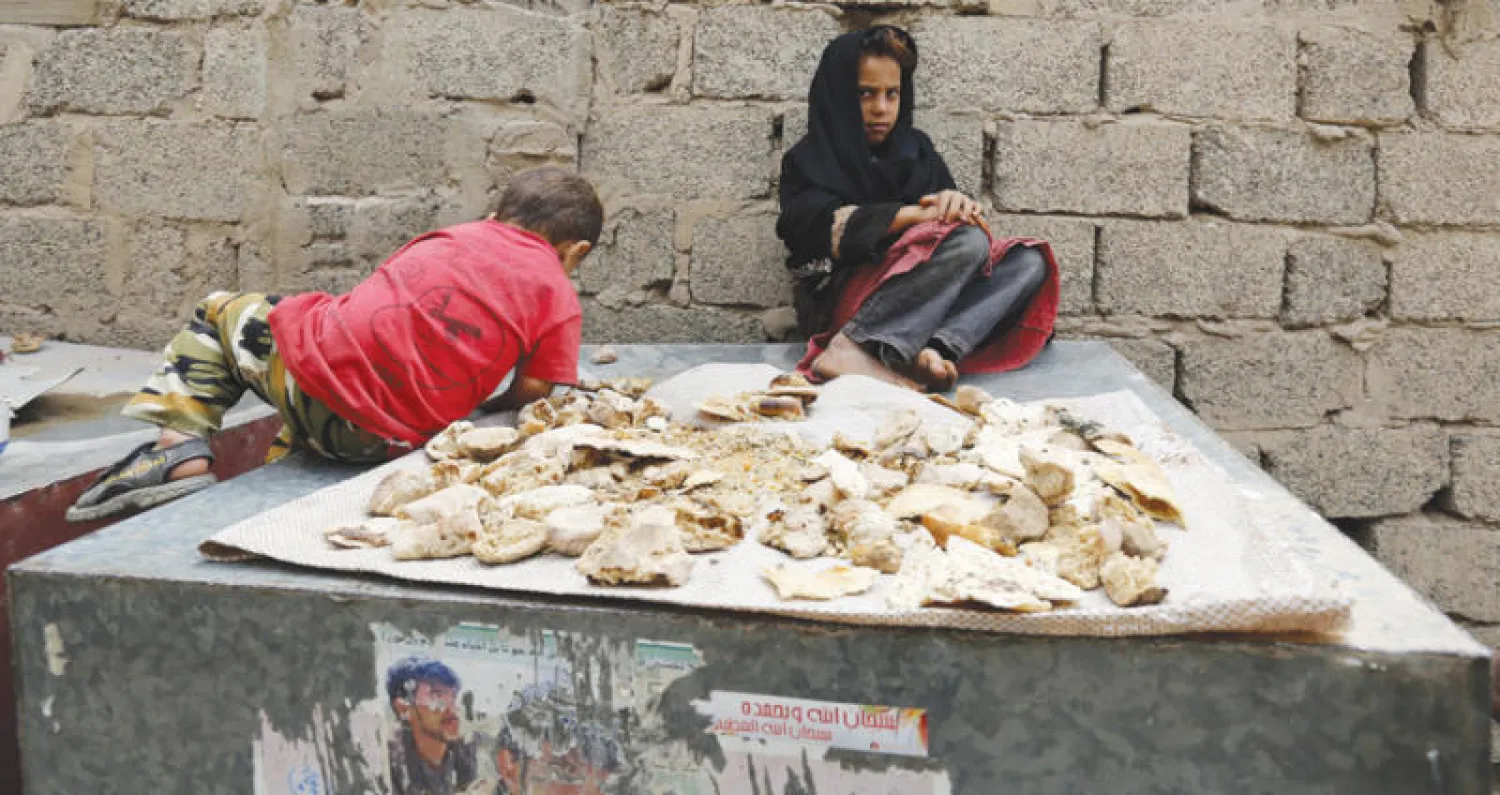 طفلان ينتظران الخبز لينشف حتى يتم تخزينه وسط أزمة صنعها الانقلاب في صنعاء (إ.ب.أ)