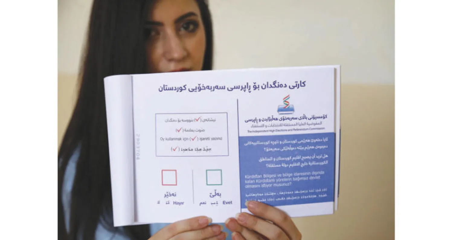 موظفة من هيئة الاستفتاء تعرض بطاقة تصويت في مركز اقتراع بأربيل امس (أ.ف.ب)