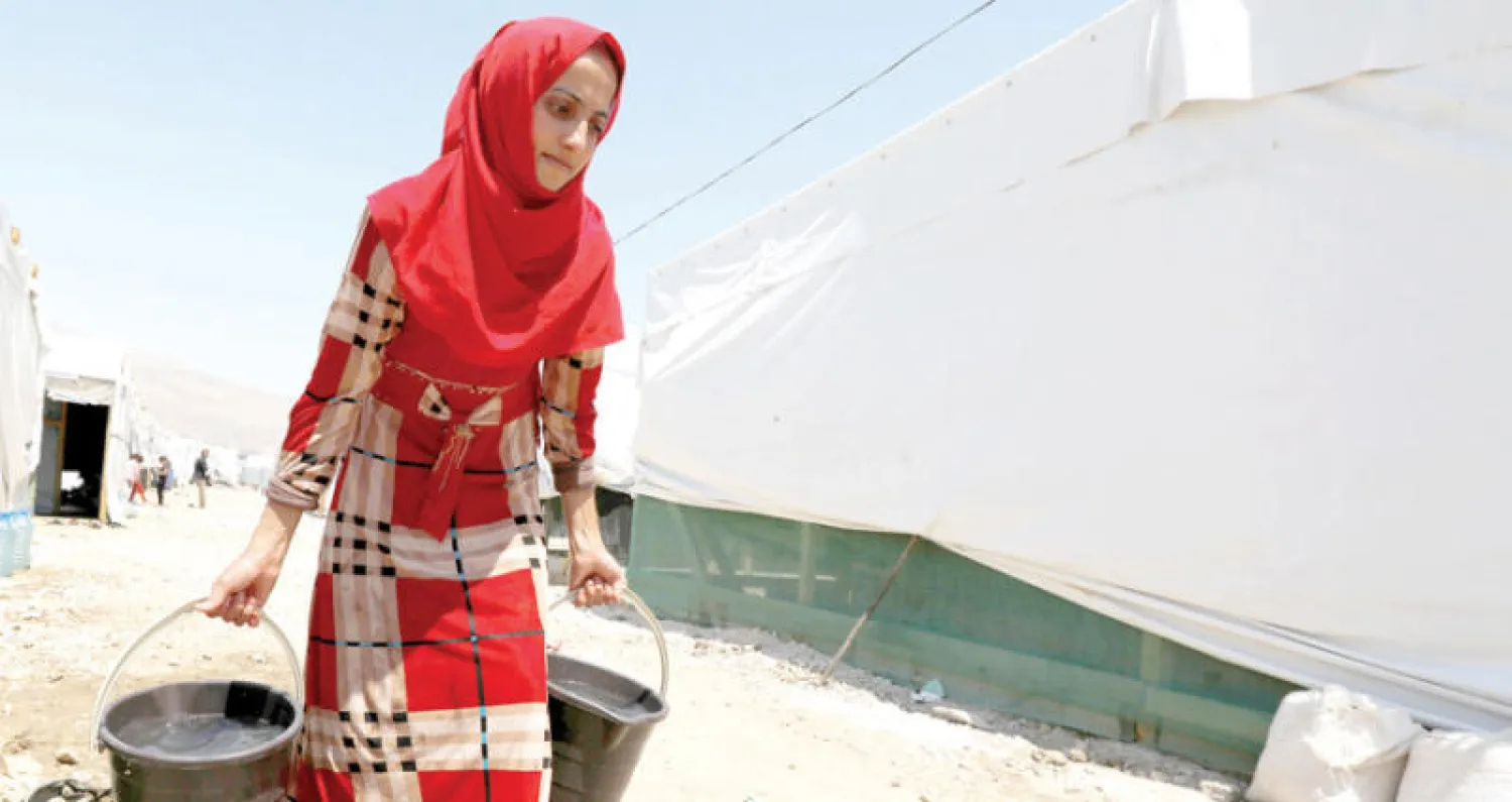 سورية تحمل مياهاً في مخيم للاجئين بالقرب من بلدة قب الياس في البقاع اللبناني (رويترز)