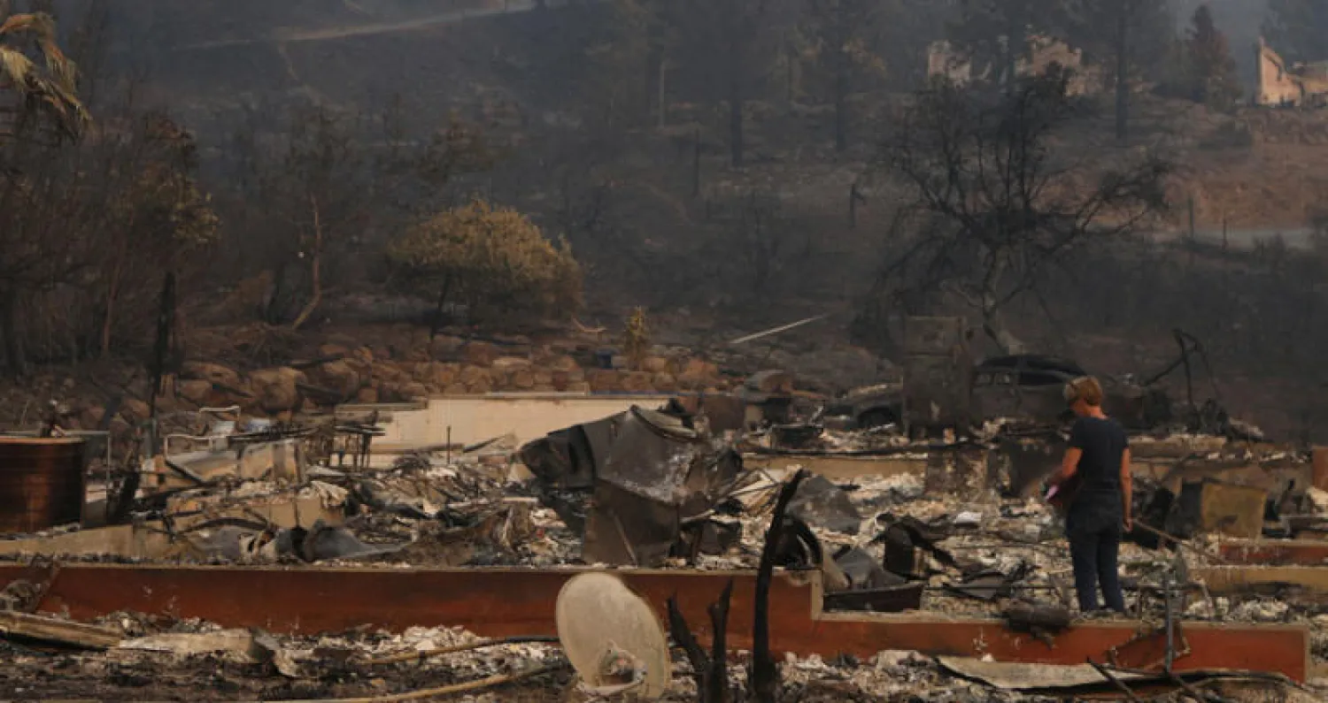 امرأة تفحص بقايا منزل أتت عليه النيران (رويترز)