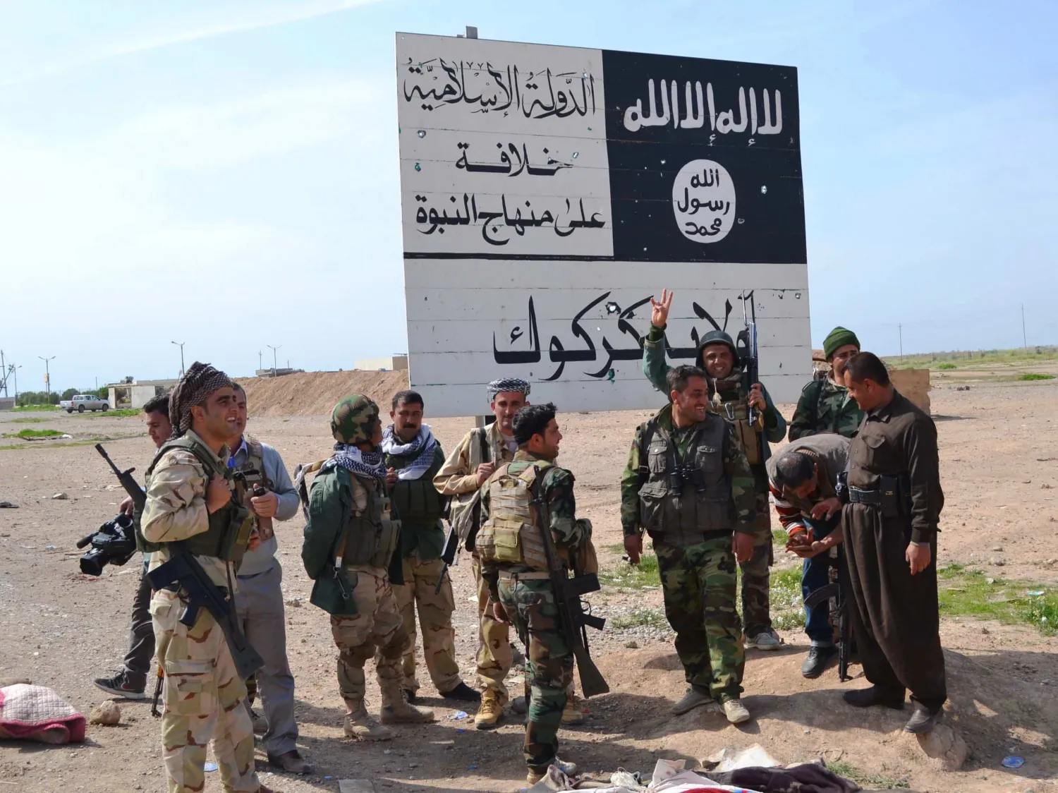 Iraqi Kurdish Peshmerga fighters stand next to an ISIS sign at the entrance to the northern Iraqi town of Hawija, south of Kirkuk on March 9, 2015. /AFP