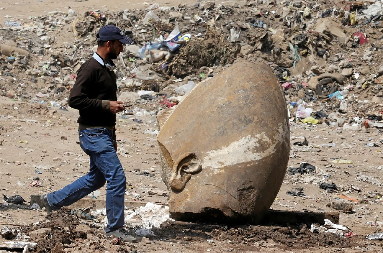 A man passes by what appears to be the head of an unearthed statue that workers say depicts King Ramesses II, in Cairo. (Reuters)