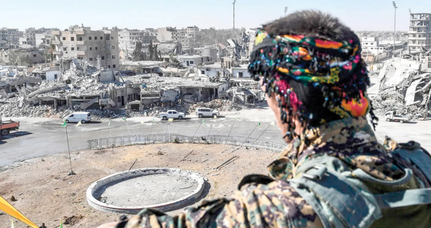 مقاتل من «قوات سوريا الديمقراطية» ينظر إلى «دوار النعيم» في الرقة أمس (أ.ف.ب)