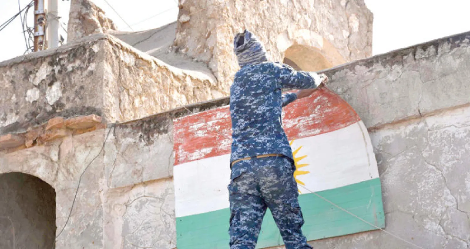 عنصر في الشرطة الاتحادية العراقية يزيل علم كردستان من مبنى في آلتون كوبري في أقصى شمال محافظة كركوك أمس (أ.ف.ب)