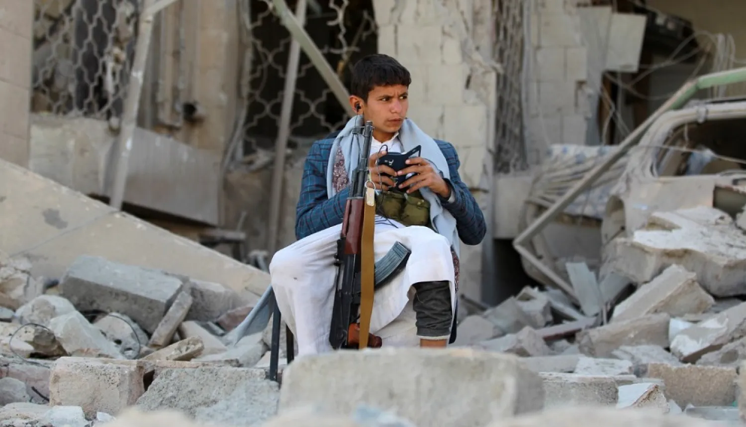 An armed Yemeni youth sits amid the rubble of a damaged house in the capital Sana’a. (AFP)