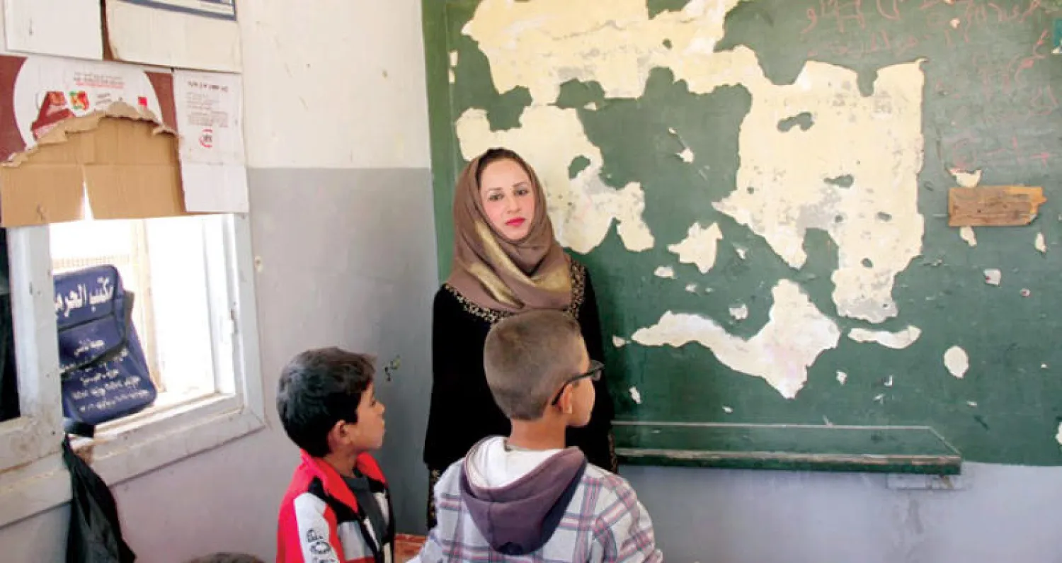المعلمة سحر تقف أمام تلميذين ولوح مدرسي شبه مدمر في حي الجزرة بالرقة