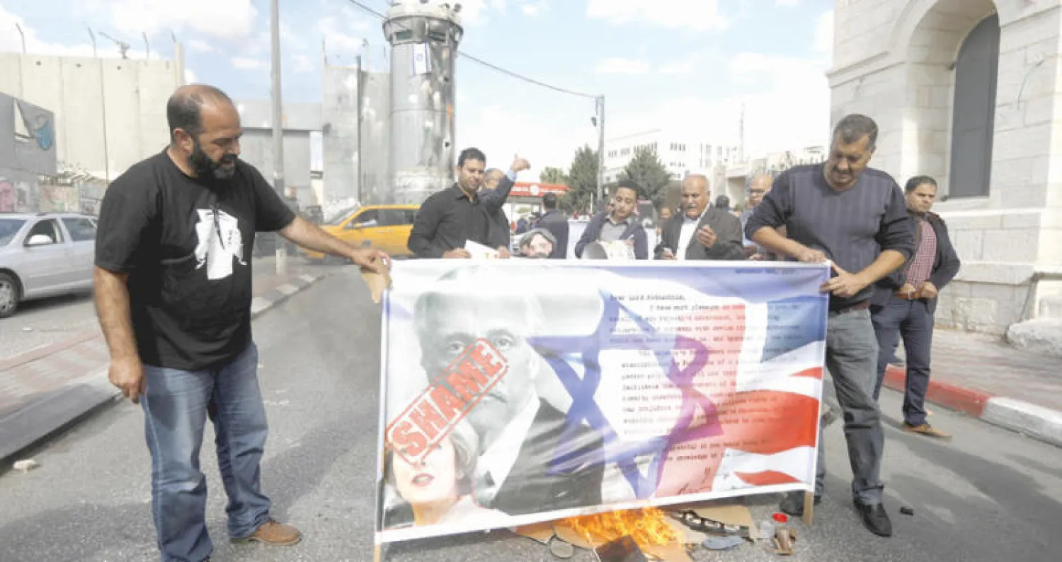 متظاهرون في بيت لحم يحرقون لافتة عليها علما إسرائيل وبريطانيا وصورة لماي واللورد بلفور (إ.ب.أ)