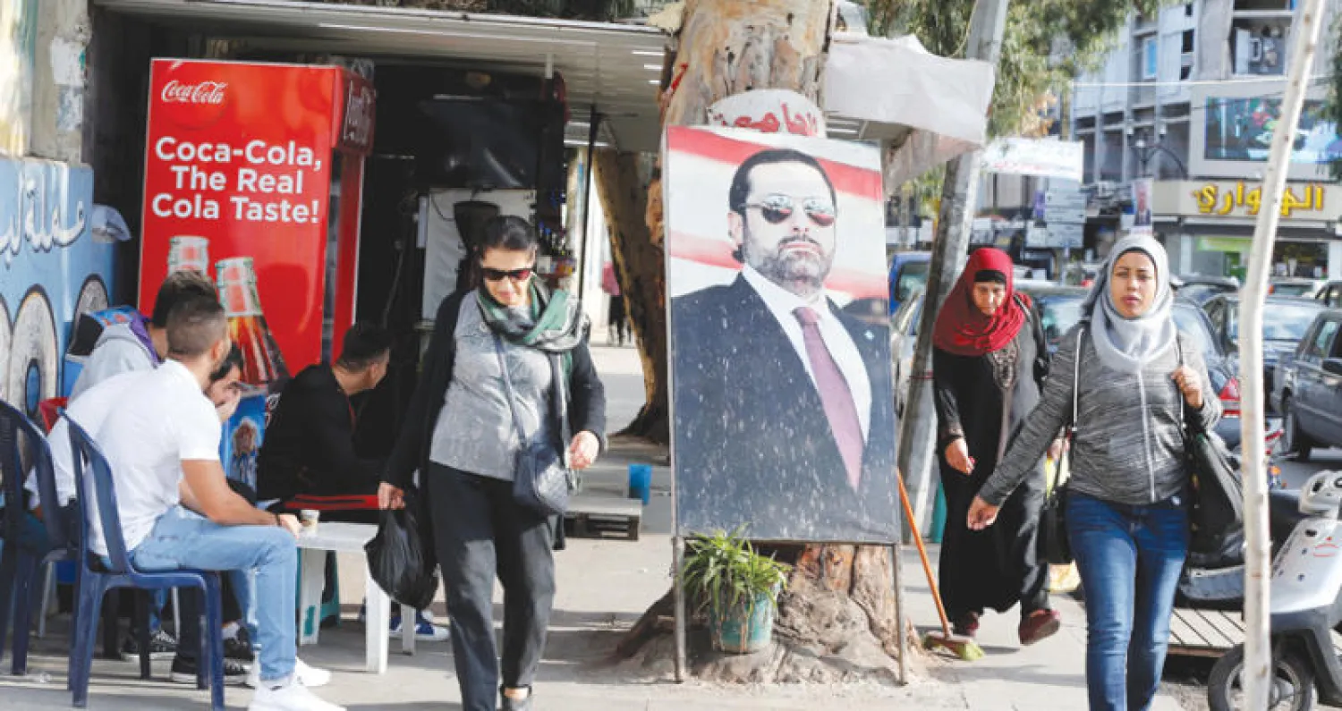 مارة يعبرون بجانب صورة رئيس الحكومة المستقيل في طريق الجديدة ببيروت أمس (رويترز)