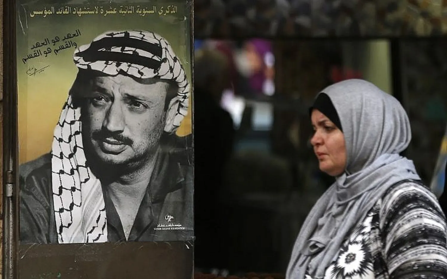 A Palestinian woman walks past a portrait of Yasser Arafat at the start of celebrations marking the 13th anniversary of his death, in the West Bank city of Ramallah, on November 9, 2017. (AFP Photo/Abbas Momani
