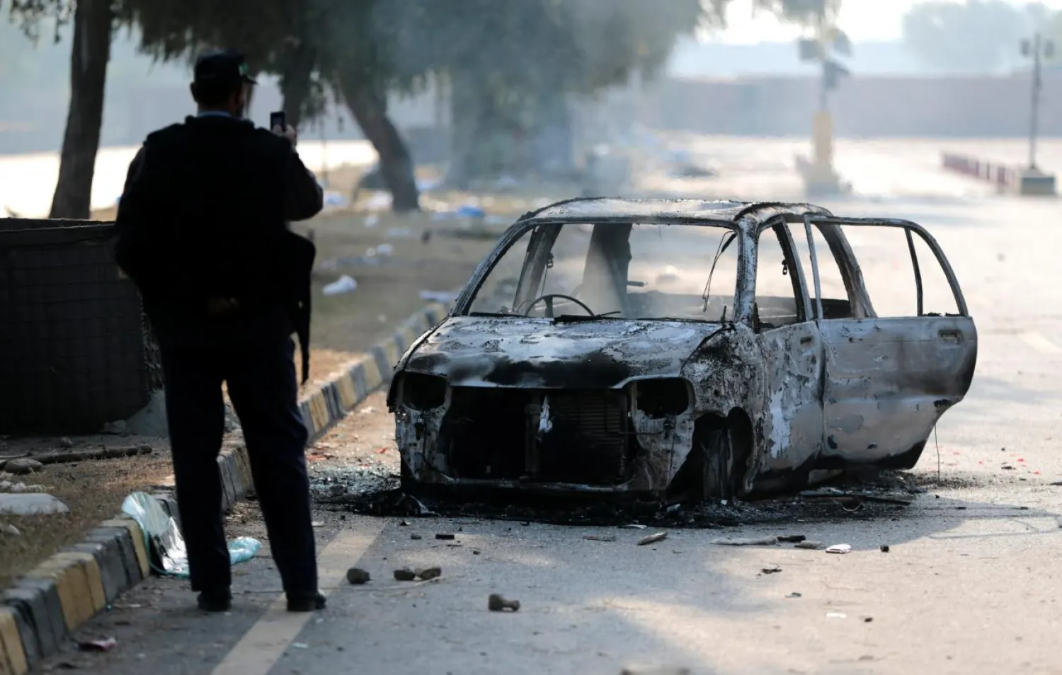 A policeman takes a picture of a car burned during clashes near the Faizabad junction in Islamabad, Pakistan November 26, 2017. REUTERS/Caren Firouz
