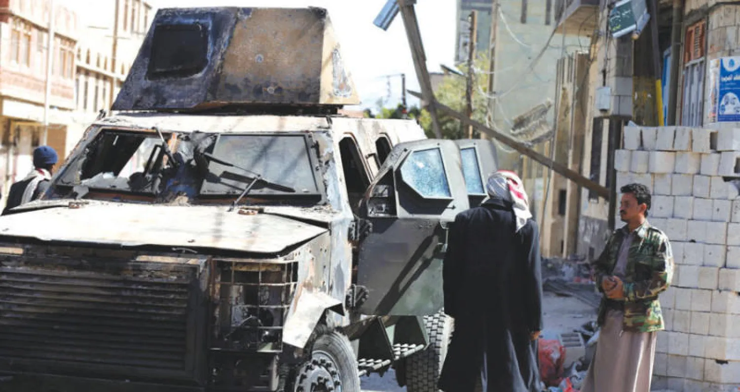 يمنيون ينظرون إلى عربة عسكرية تحطمت في معارك صنعاء (رويترز)