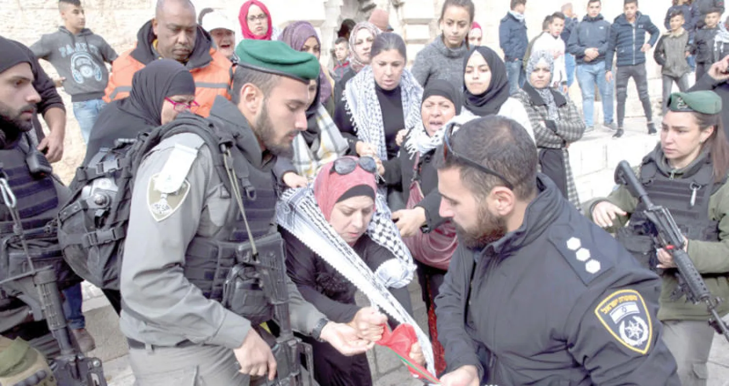 جنديان إسرائيليان يحاولان منع امرأة من رفع العلم الفلسطيني خلال مظاهرة نظمت أمس في القدس القديمة (إ.ب.أ)
