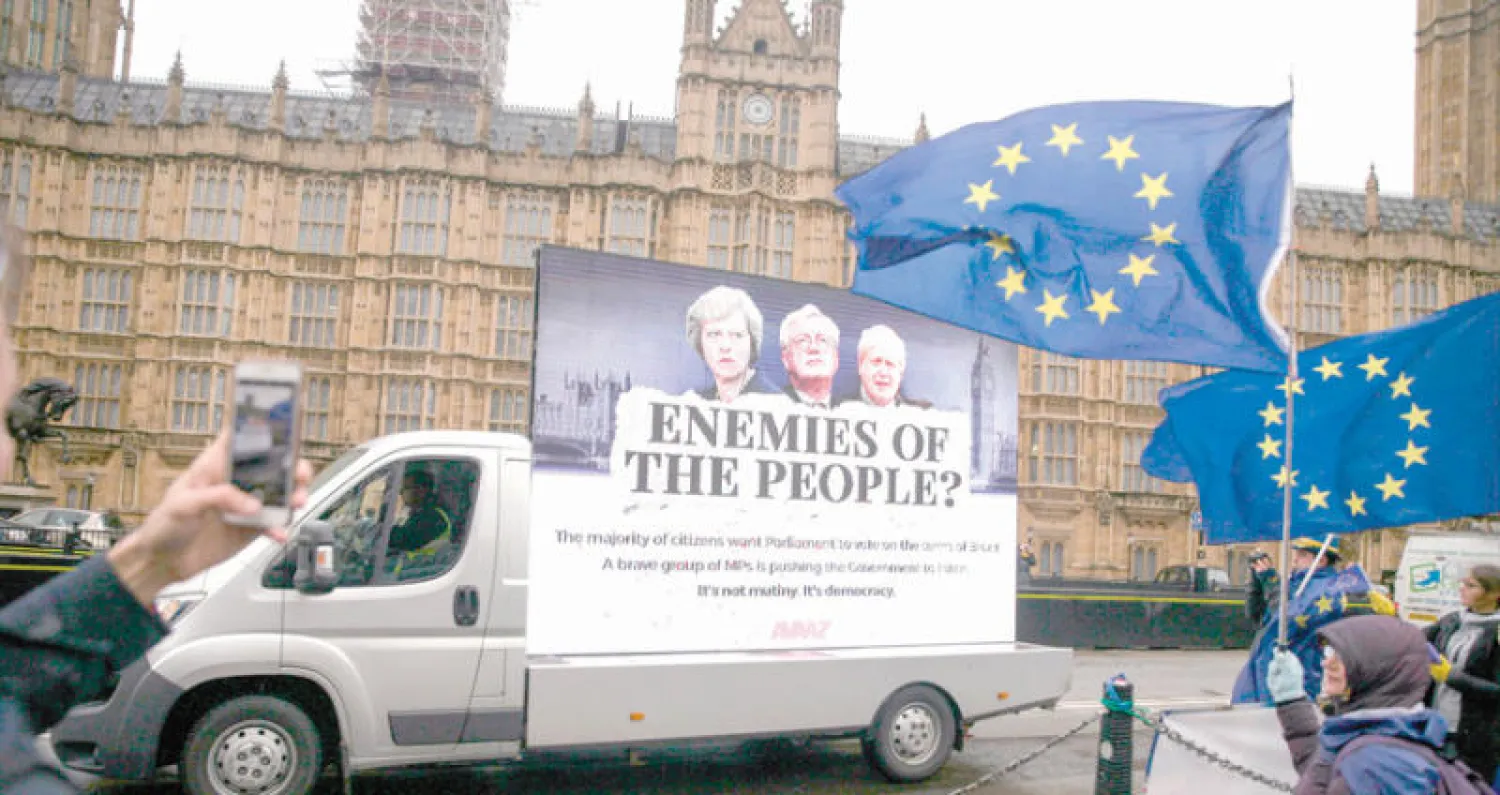 محتجون ضد خروج بريطانيا من الاتحاد الأوروبي يرفعون أمام البرلمان يافطة كتب عليها «أعداء الشعب» وعليها صور رئيسة الوزراء ووزير الخارجية ووزير «بريكست» (أ.ف.ب)