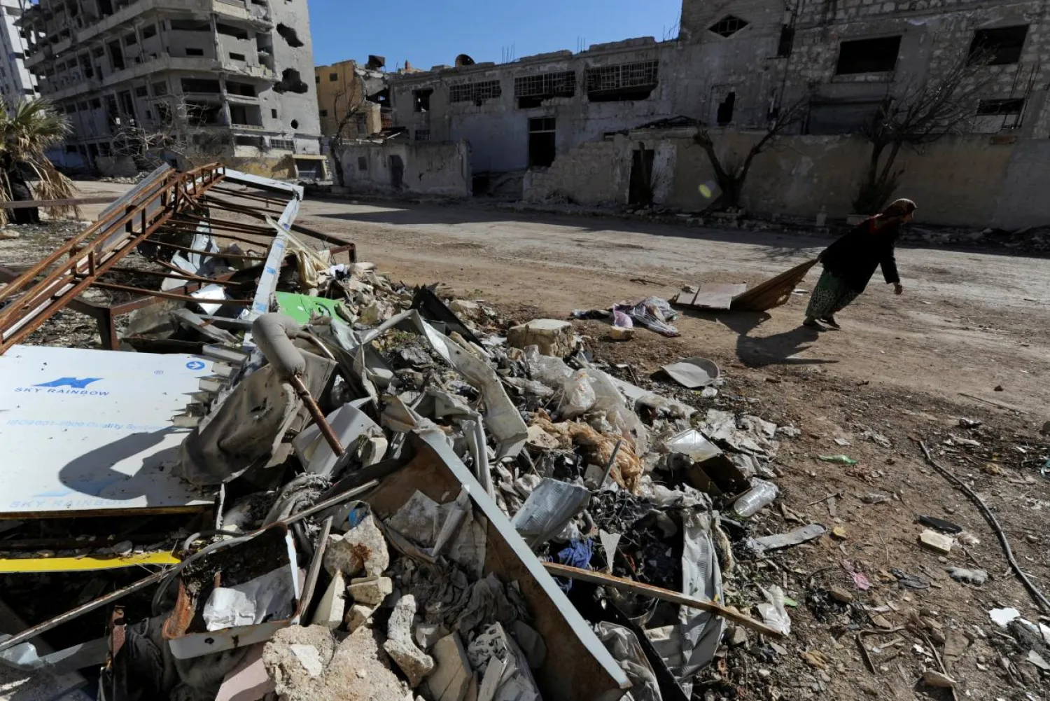 A woman walks past debris along a street in Aleppo's Belleramoun Industrial Zone, Syria February 2, 2017. Reuters