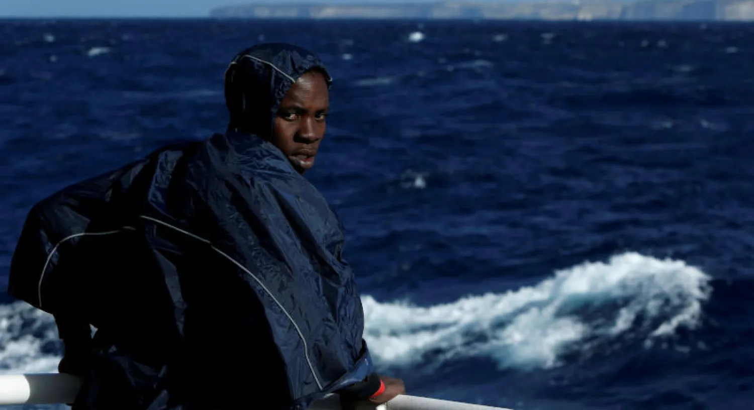 مهاجر يقف على سطح سفينة بعد عملية إنقاذ قبالة السواحل الليبية (رويترز)