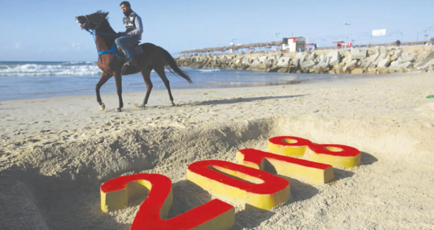 شاب على حصانه يمر أمام كتابة على الرمل لعام 2018 على شاطئ غزة (أ.ف.ب)