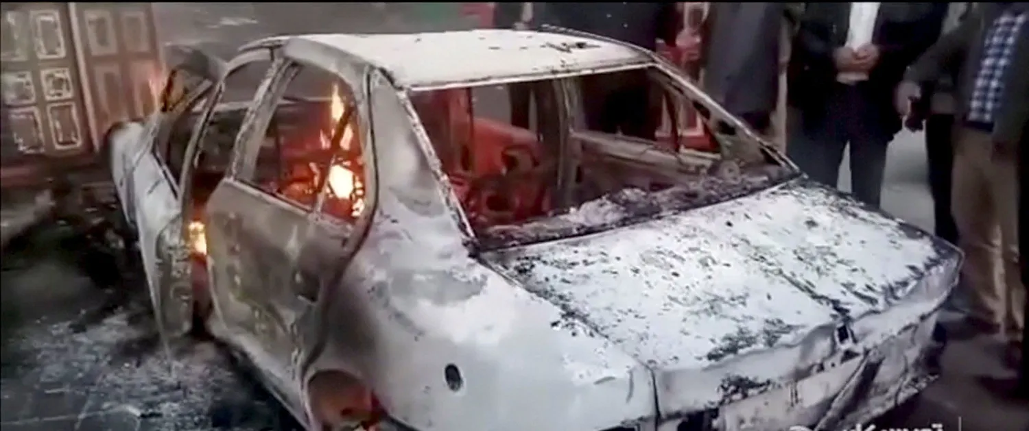 مجموعة من الأشخاص يقفون بالقرب من سيارة محترقة في مدينة تويسركان بإيران (رويترز)