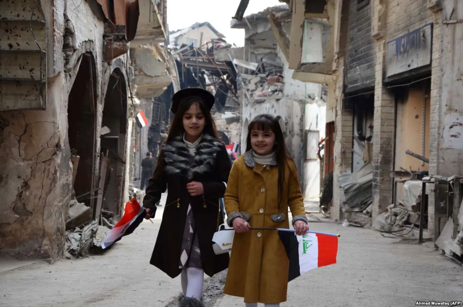 Iraqi girls walk holding their national flag towards a ceremony for the re-opening of the Bab al-Saray market in the old city of Mosul on January 11, 2018. Ahmad MUWAFAQ / AFP