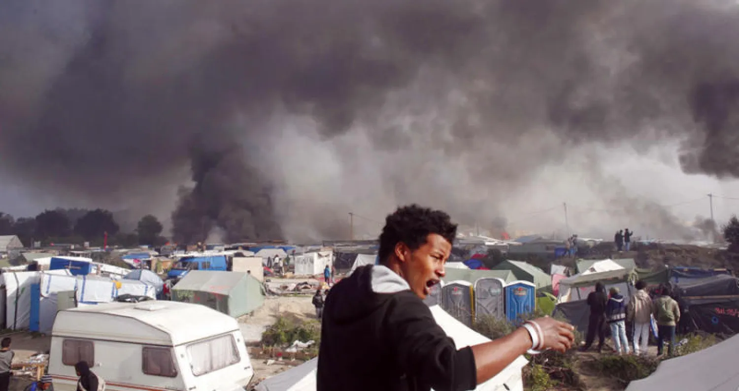 صورة أرشيفية لمهاجر يقف في «مخيم الغابة» بكاليه الفرنسية في أكتوبر الماضي (أ.ب)