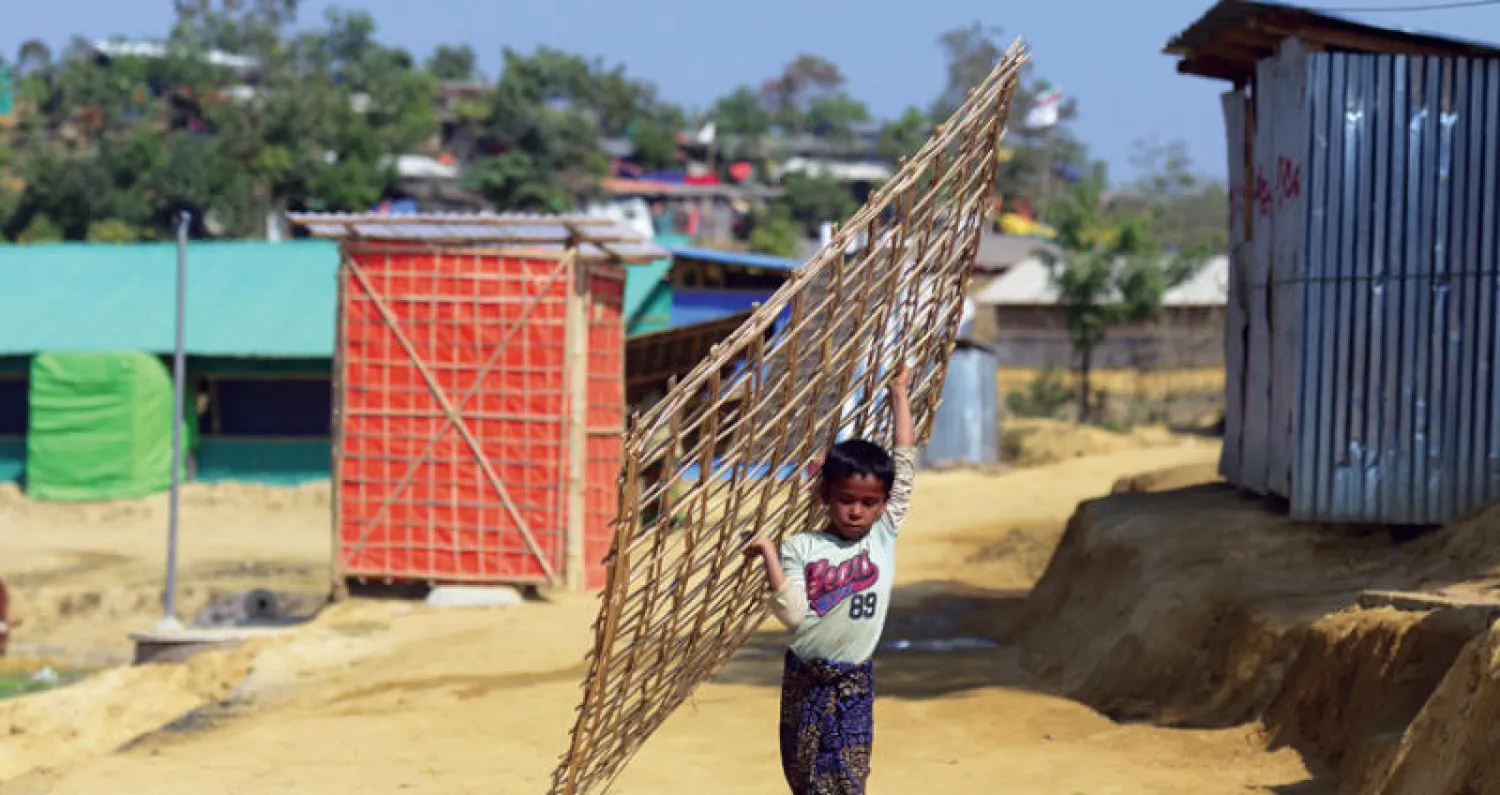 طفل من الروهينغا يحمل قطع خيزران لبناء منزل في مخيم للاجئين في منطقة أوخيا ببنغلاديش أمس (أ.ف.ب)