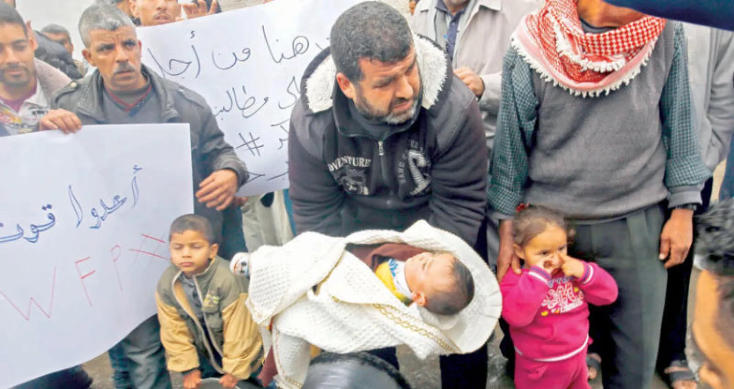 أب وأطفاله أمام مكتب الأمم المتحدة في غزة ضمن مجموعات تحتج على قطع المساعدات (أ.ف.ب)