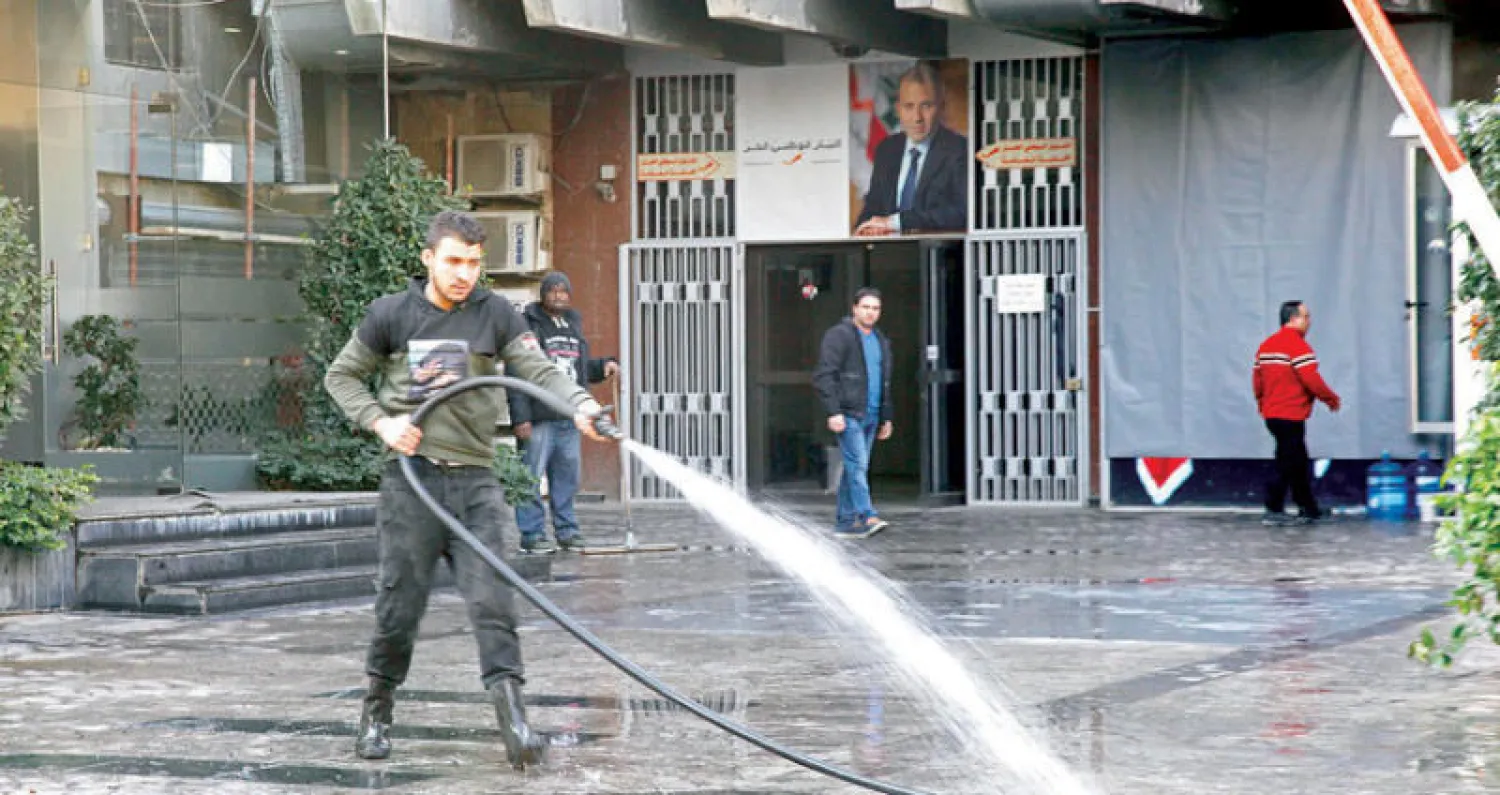 أحد حراس مقر «التيار الوطني الحر» ينظف آثار الإطارات التي أشعلها مناصرو «حركة أمل» أول من أمس (الشرق الأوسط)