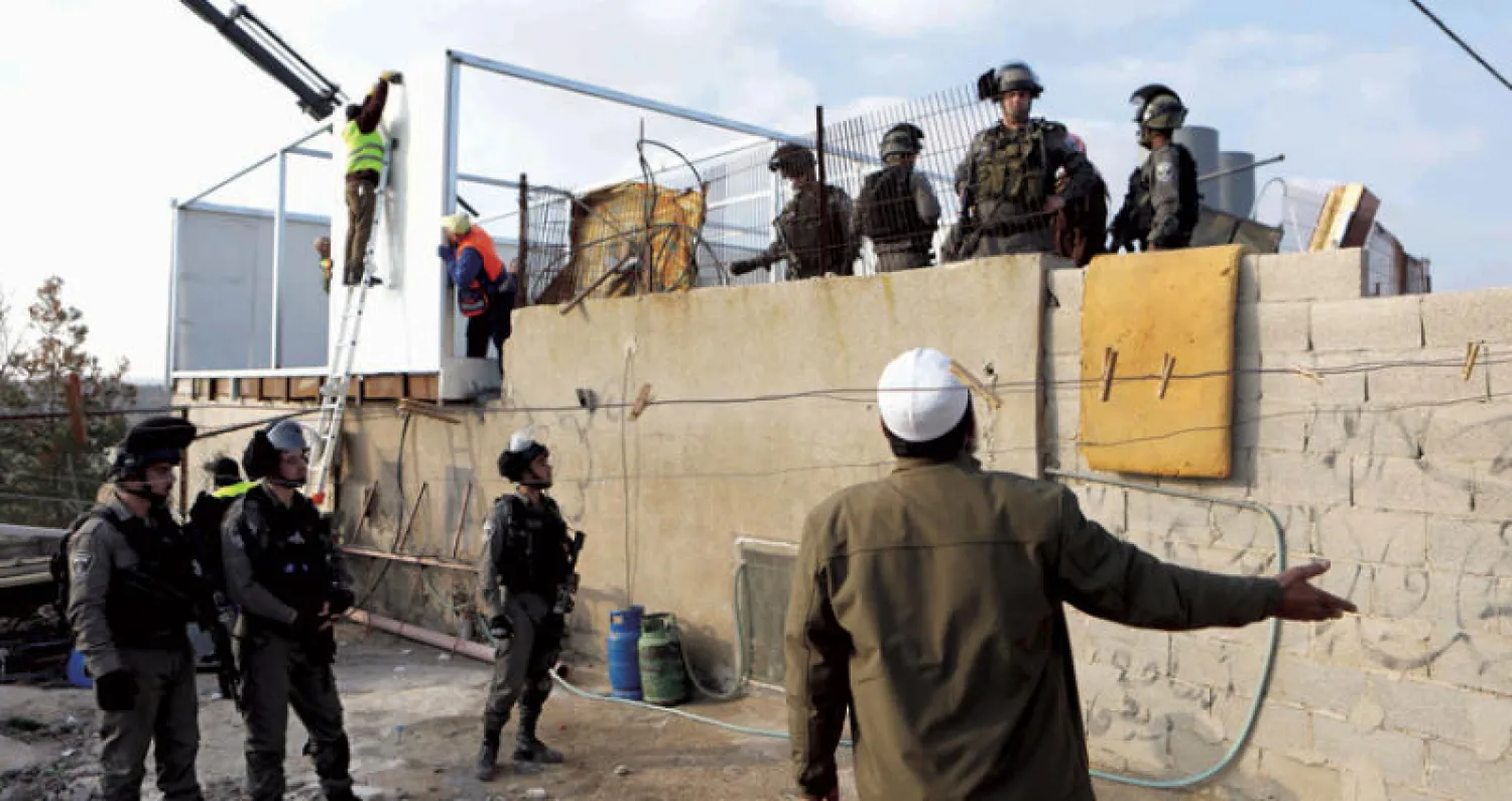 فلسطيني يجادل جنودا إسرائيليين أثناء حراستهم عملية تدمير بيته في قرية ياتا بالضفة الغربية (إ.ب.أ)