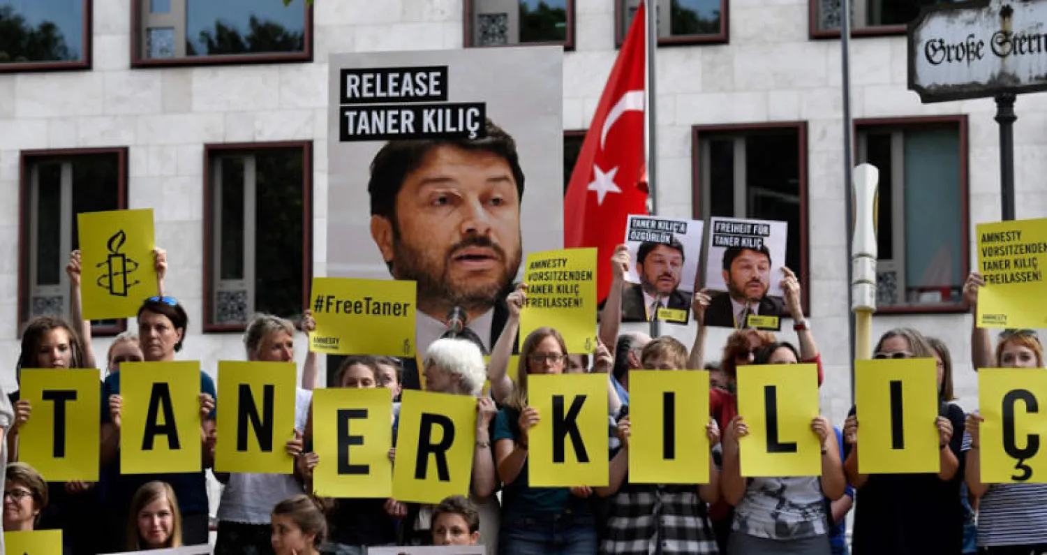 نشطاء من «منظمة العفو الدولية» يحملون صوراً لمسؤول فرعهم في تركيا تانر كيليتش ويحتجون أمام السفارة التركية في برلين على احتجازه (أ.ف.ب)