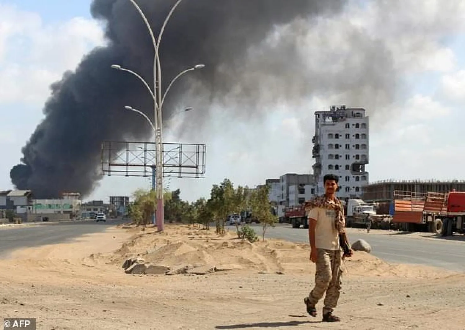 A fighter from the separatist Southern Transitional Council walks with smoke billowing in the background in the government's de facto capital Aden (AP)
