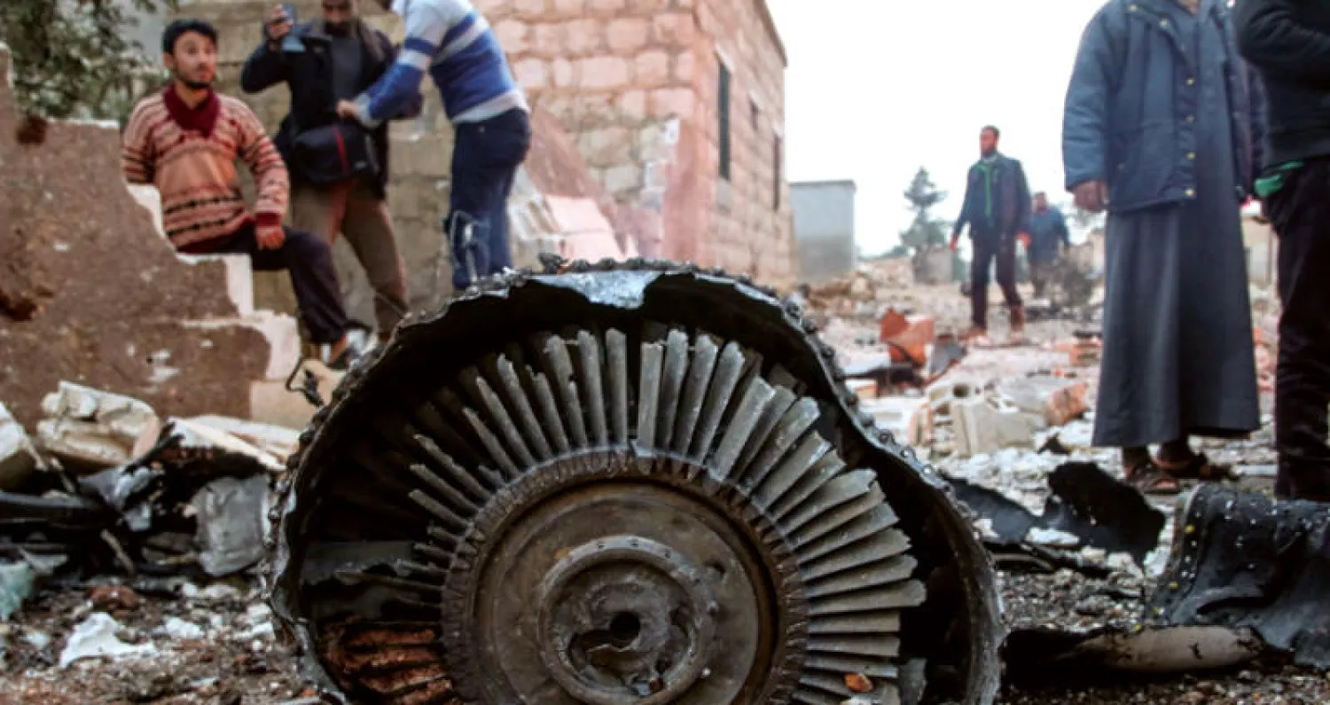 سكان محليون في محافظة إدلب يقفون أمام حطام طائرة سوخوي-25 الروسية أول من أمس  (إ.ب.أ)