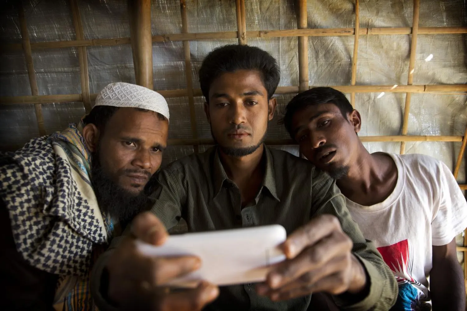 In this Jan. 14, 2018 photo, Rohingya Muslim refugee Mohammad Karim, 26, center, shows a mobile video of Gu Dar Pyin’s massacre to other refugees in Kutupalong refugee camp, Bangladesh. (Manish Swarup/Associated Press) 