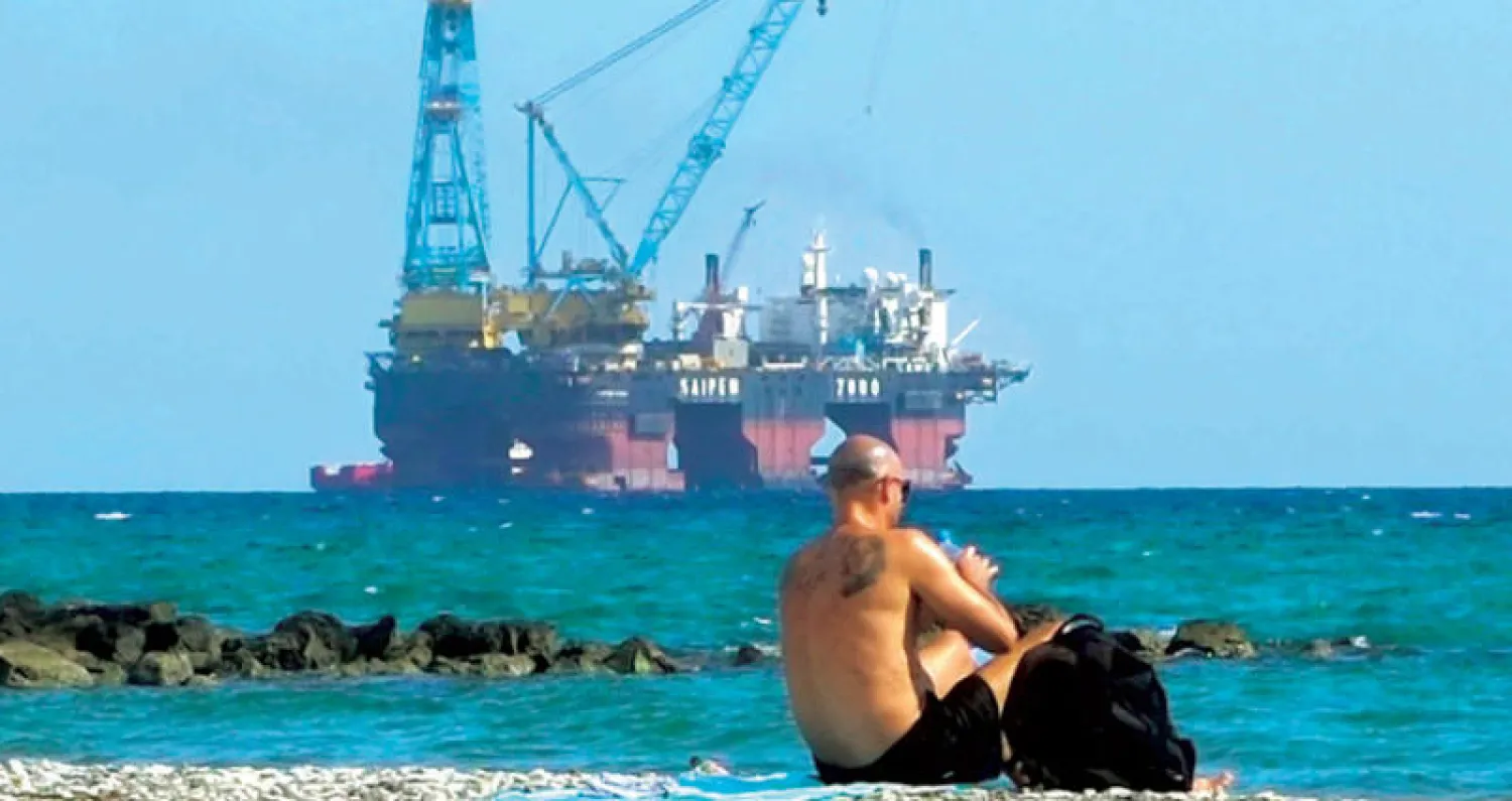 رجل يجلس على الشاطئ في لارنكا  قبالة منصة للتنقيب عن المحروقات (ا.ب)