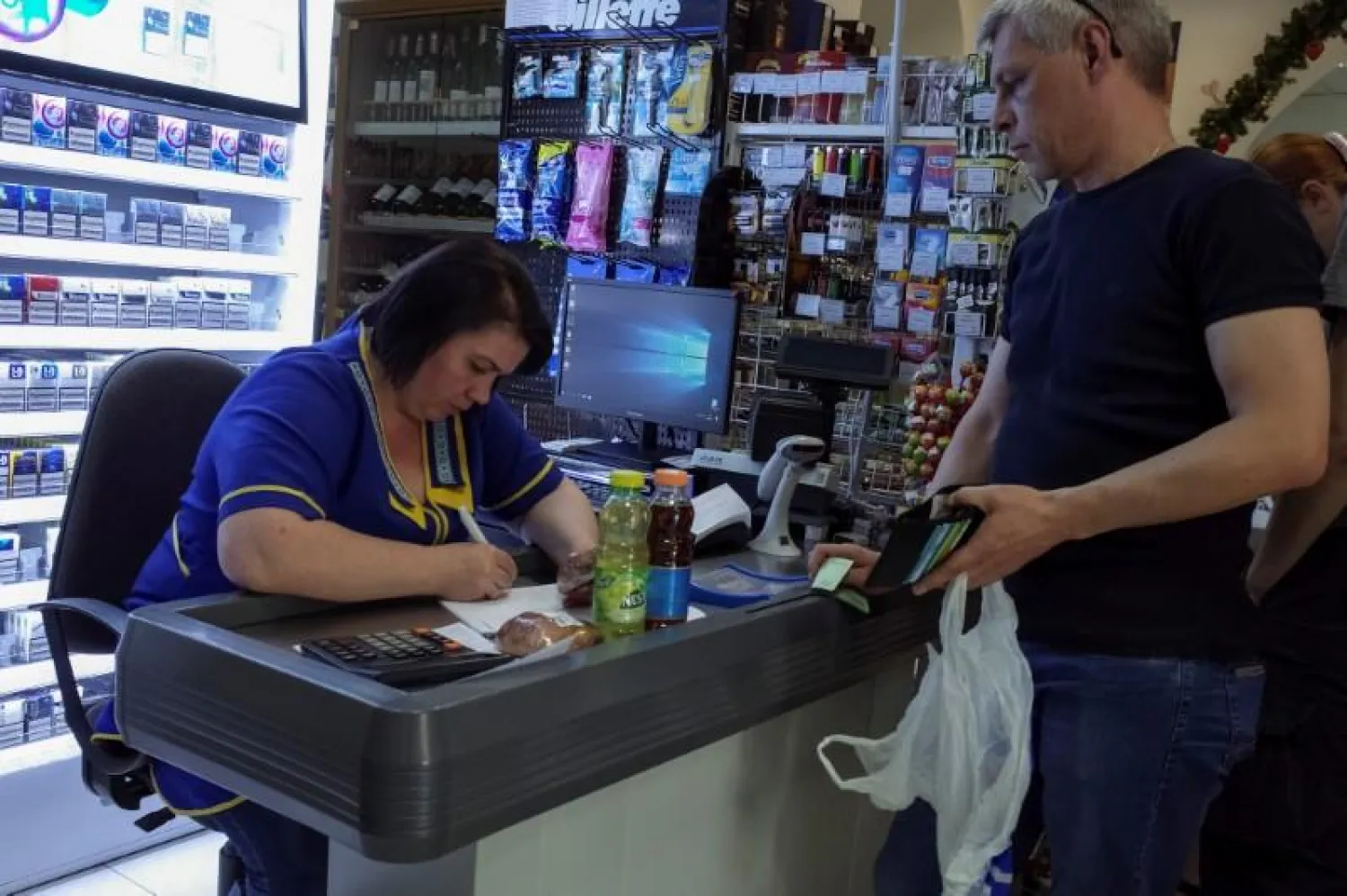 A customer waits while a cashier writes out a purchase receipt for store records, as many business have turned off their digital tills after cases of cyber attacks on business, at a store in Kiev, Ukraine, June 28, 2017. REUTERS/Gleb Garanich