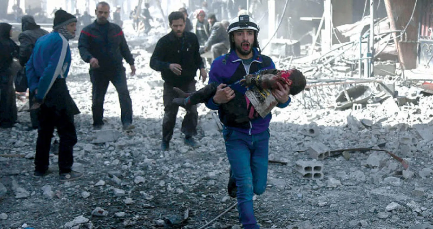 عنصر في الدفاع المدني يحمل طفلا جريحا اُنتشل من  تحت أنقاض منزل دمره قصف النظام على حمورية في غوطة دمشق أمس (أ.ف.ب)