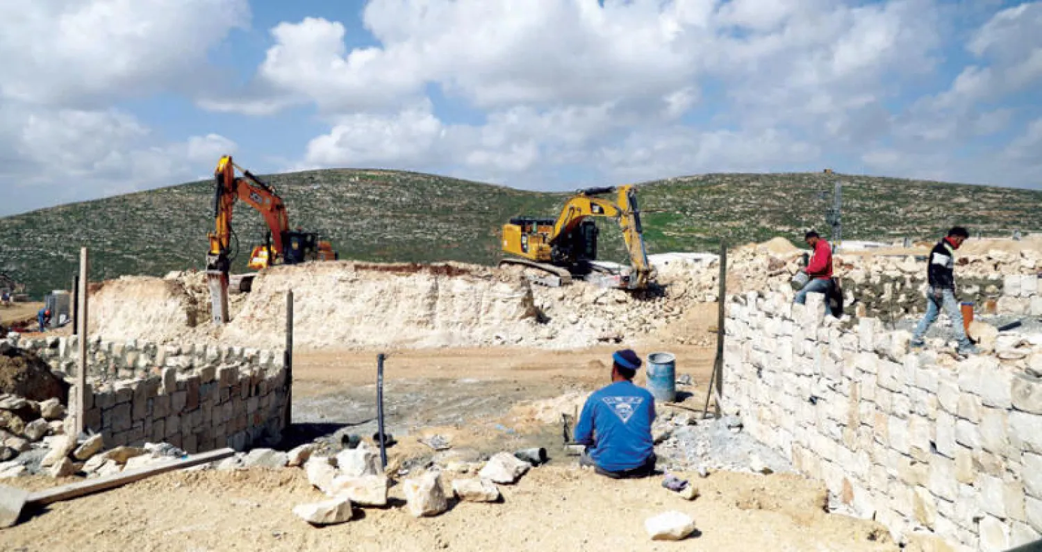 عمال في موقع مستوطنة عميحاي بالضفة الغربية وجرافات تمهد الأرض للبناء (رويترز)