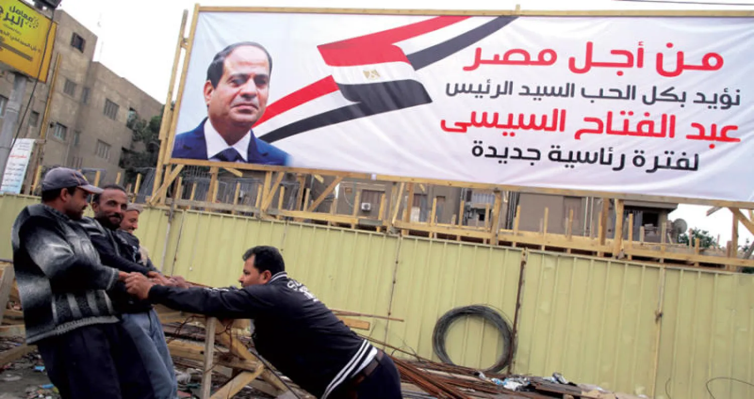 عمال مصريون يعملون أمس في أحد المواقع تحت الانشاء ويبدو ملصق ضخم تأييدا للسيسي (إ ف ب)