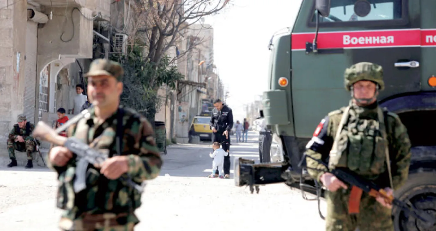 عنصر روسي (يمين) وآخر سوري على معبر مخيم الوافدين في غوطة دمشق أمس (رويترز)