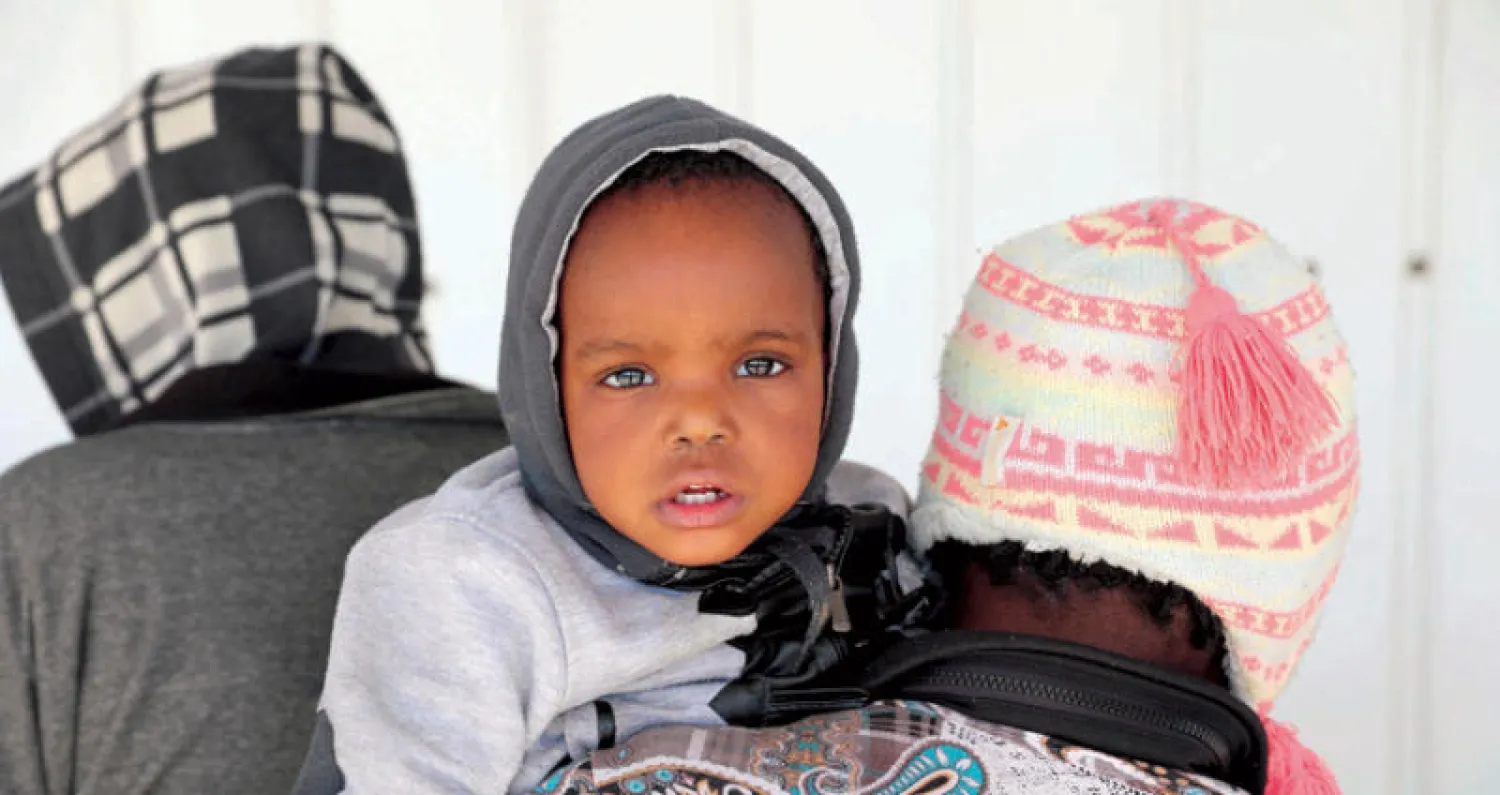 مهاجر يحمل طفلاً في قاعدة عسكرية في طرابلس بعد يوم من إنقاذ البحرية الليبية مجموعة من المهاجرين يوم السبت (رويترز)