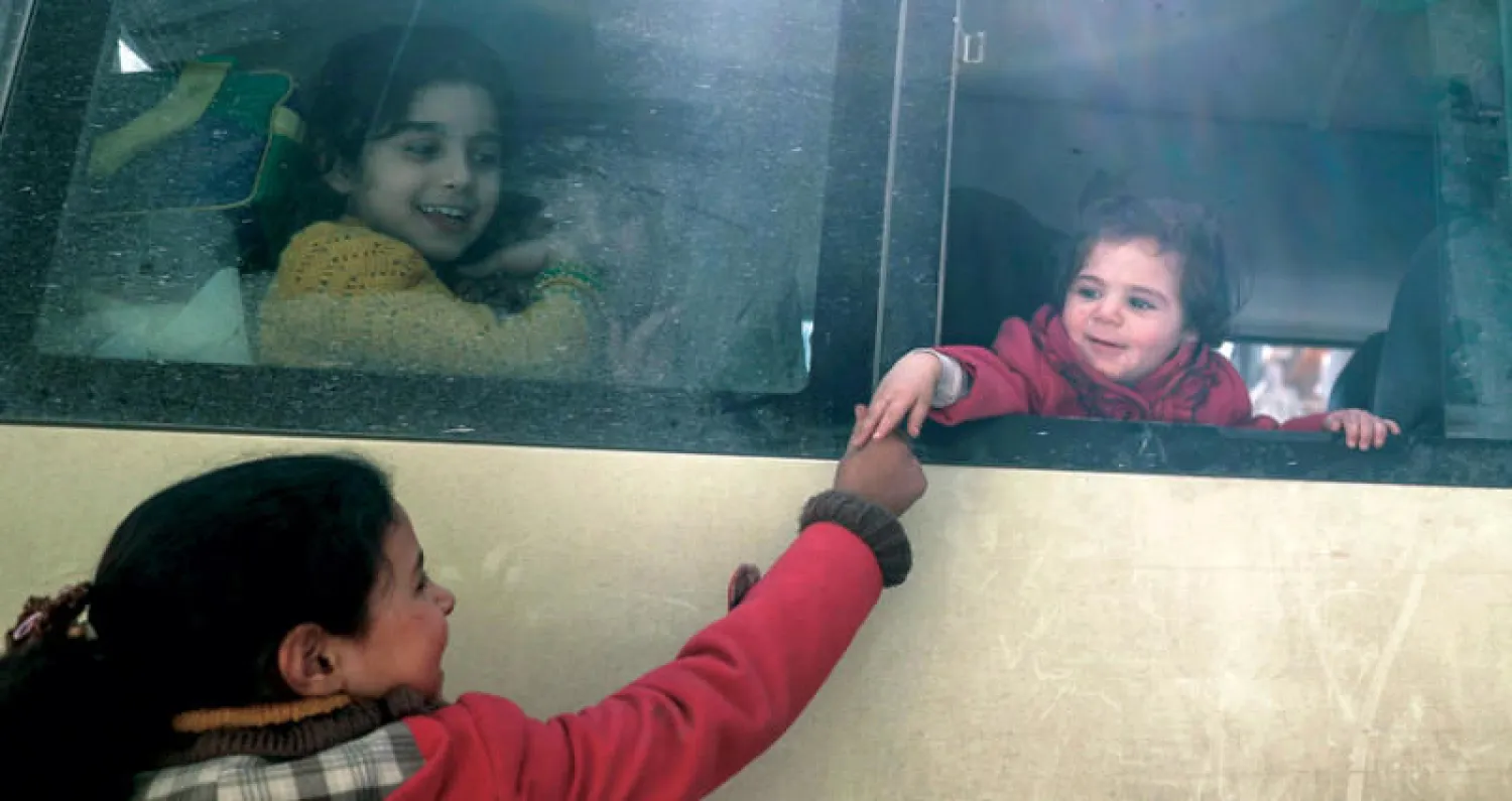 وداع طفلتين في الغوطة قبل تحرك الحافلة التي أقلت الدفعة الثانية من المرضى أمس (إ.ب.أ)