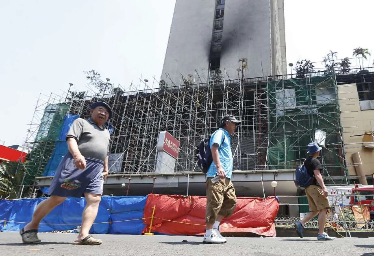 Foreign hotel guests walk past the burnt Manila Pavilion Hotel and Casino to retrieve their belongings Monday, March 19, 2018, in Manila, Philippines. (Bullit Marquez/Associated Press)